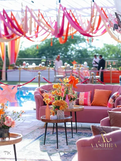 A comfortable and stylish lounge area by the pool, with pink sofas, colorful cushions, and tables adorned with fresh orange flowers.
