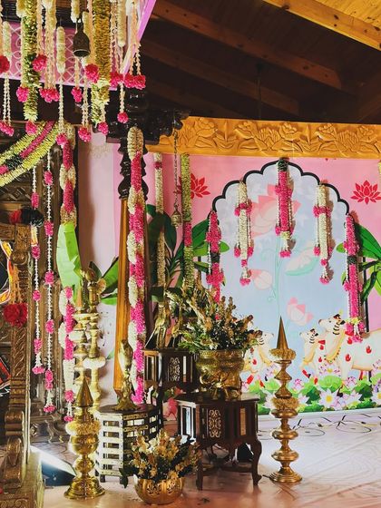 This view highlights the beautiful interplay of light and color in the naming ceremony decor. The brass lamps glow against the pink backdrop, illuminating the intricate floral work.