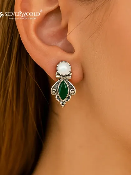 This close-up shows the fine craftsmanship of our gemstone earrings. Here, a marquise-cut green stone is paired with a classic pearl, all set in an antique-finish silver base, creating a look of understated luxury.