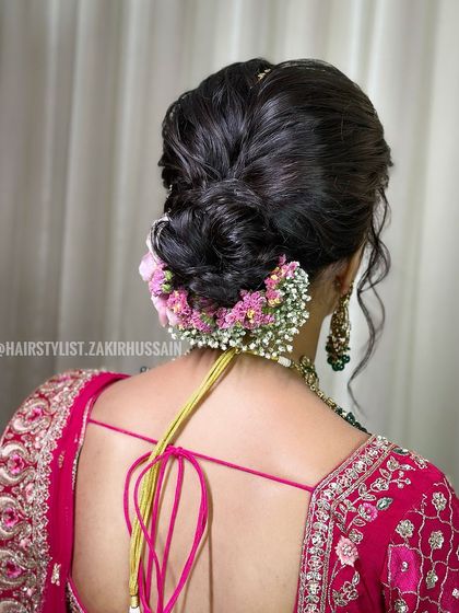 A soft and romantic low bun, elegantly decorated with a line of fresh pink flowers and baby's breath. This style is perfect for a daytime event or a pre-wedding function.