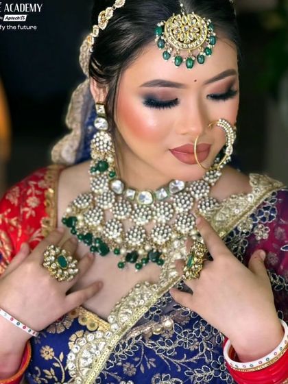 A bride wearing a heavy Kundan necklace with large uncut stones and green bead drops. The look is completed with a large maang tikka and matching rings.