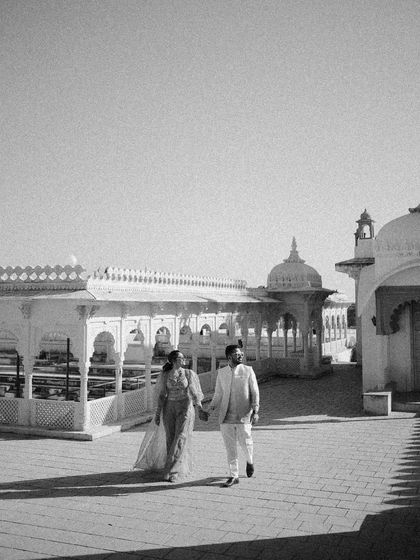 A classic black and white walking shot, capturing the couple's movement and connection. The strong shadows and heritage architecture create a beautiful, timeless scene.