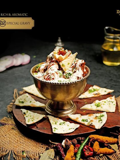 Witness the rich and aromatic Chicken DZ Special Gravy. This is our signature chicken curry, served in a traditional brass bowl with naan triangles.