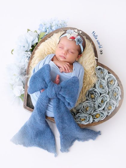 A heart-shaped basket filled with blue flowers provides a beautiful frame for this sleeping newborn. The large blue bow adds a touch of whimsy to this sweet setup.