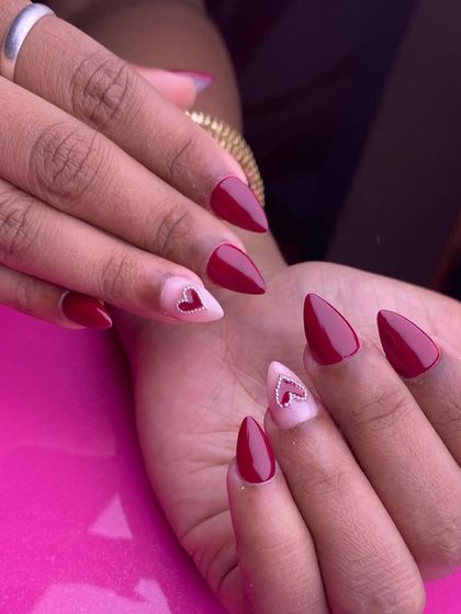 A sharp and sweet Valentine's look. This stiletto nail set features a bold red polish with accent nails showcasing a tiny, sparkling rhinestone heart on a soft pink base.