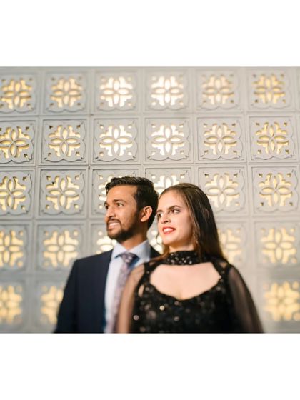 A stylish portrait of the couple at their cocktail party, posing against a modern, patterned wall.