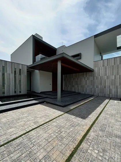 The grand entrance of Rosewood Farmhouse, featuring an oversized covered porch and a serene water feature. The design is aligned with Vastu principles and uses a warm palette of wood and grey stone to create a powerful first impression.