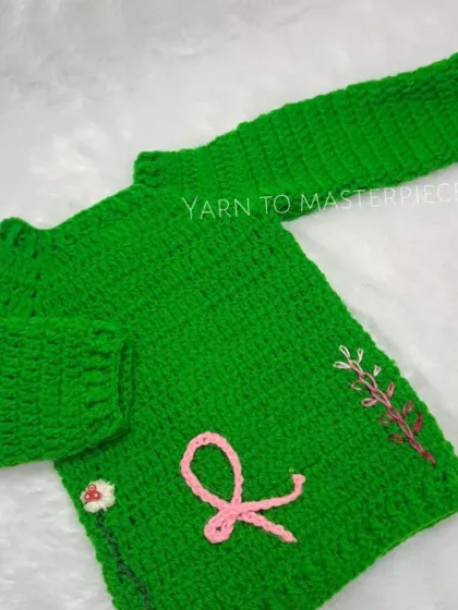 This vibrant green sweater is made with soft yarn and features delicate, hand-embroidered floral details and a simple ribbon, offering a touch of nature-inspired charm.