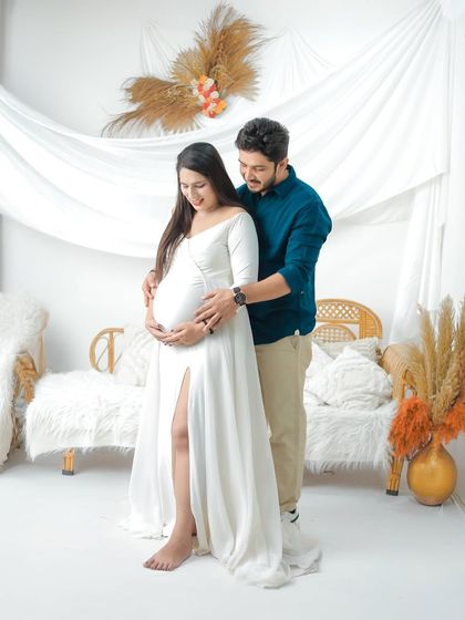 A tender moment between an expecting couple in our bright, white studio. The partner stands behind his wife, gently holding her bump as she stands in a simple yet elegant white gown.