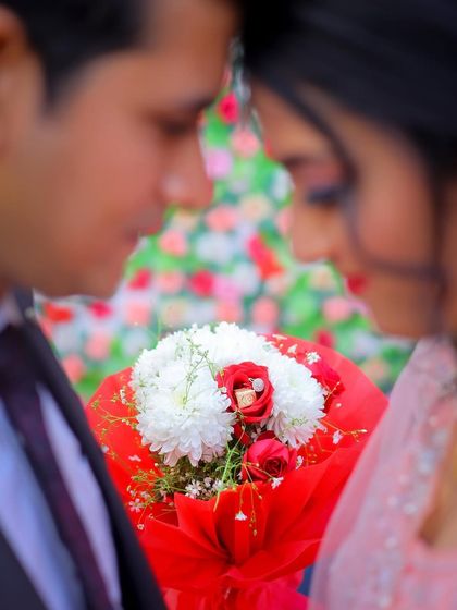 A creative shot focusing on the ring inside a bouquet, with the couple blurred in the background.