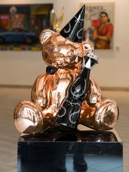 The "Let's Party Teddy" in rose gold chrome, a symbol of arrested development where childhood comfort meets celebratory excess. This fiber sculpture is frozen in a state of perpetual festivity.
