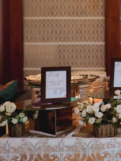 An elegant table setup for a birthday, featuring framed menus for dishes like Som Tam Salad. Small floral arrangements in wooden pots add a touch of class to the display.