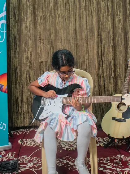 A young girl in a colorful dress plays an electric guitar at our HSR open mic session.