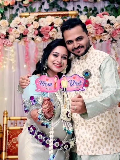 A joyful couple poses with 'Mom' and 'Dad' props in front of a stunning floral backdrop during their baby shower, showcasing how I blend fun photography with beautiful event decor.