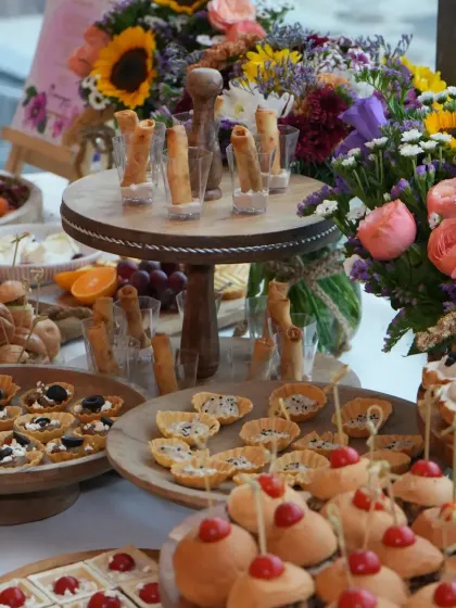 A vibrant and abundant spread for the Varnya salon launch. The table is filled with a variety of canapés, including truffle rolls and mini tarts, all beautifully arranged with fresh flowers.