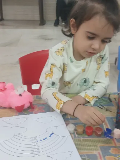 A quiet moment of concentration as a toddler paints a rainbow. We provide a calm and supportive environment where even the youngest children can focus on their creative process.