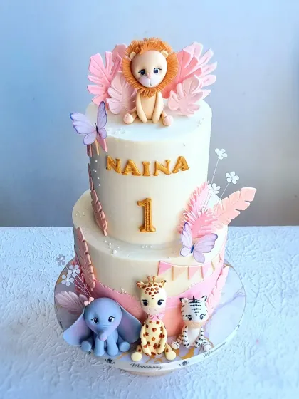 A two-tiered safari cake with a soft pink and gold color scheme. This design shows how to adapt a popular theme for a different aesthetic, using delicate colors and butterfly accents.