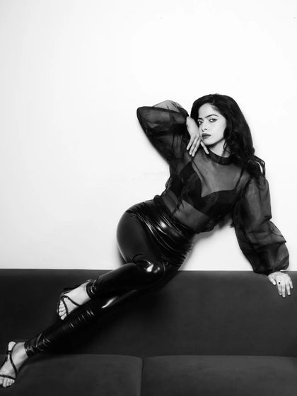 A variation of the black and white couch portrait, showing a slightly different angle. The consistent moody lighting and styling create a cohesive and strong series.