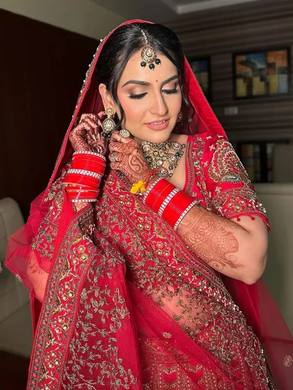 A candid moment as the bride adjusts her earring, showcasing the flawless makeup and the intricate details of her red bridal attire.