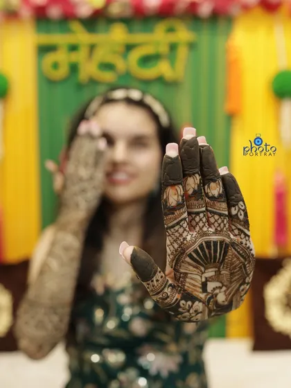A creative shot focusing on the intricate details of the bride's palm henna, with the happy bride smiling in the background.
