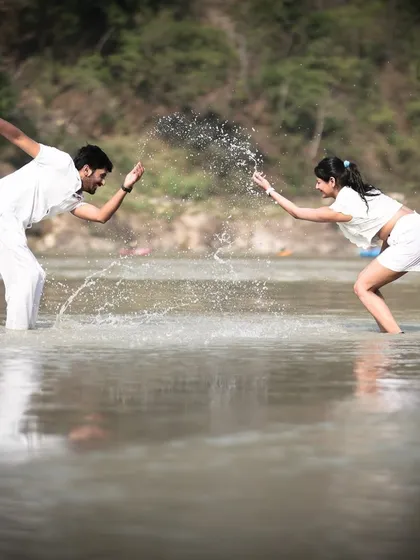 A fun, candid moment of a couple splashing each other in a river, showcasing their playful connection during their pre-wedding shoot.