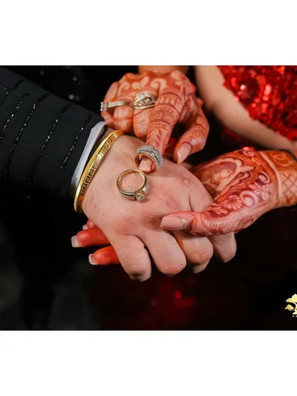 A close-up shot of the couple's hands, showcasing their engagement rings and the bride's beautiful henna.