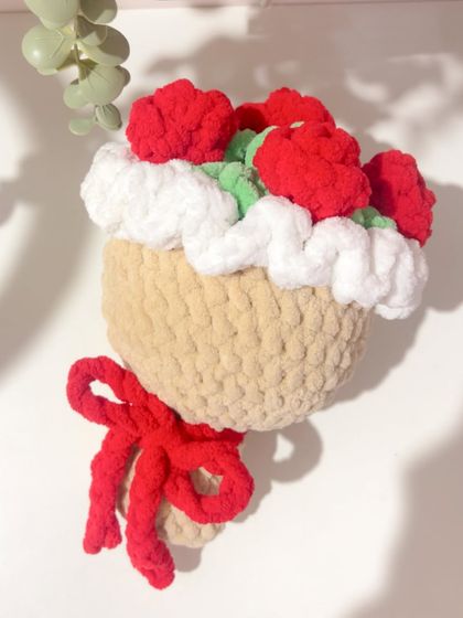 A close-up shot of my rose plush bouquet hanging as a decorative piece. The design features red roses and a fluffy white border, all crocheted from soft, thick yarn and tied with a red bow.