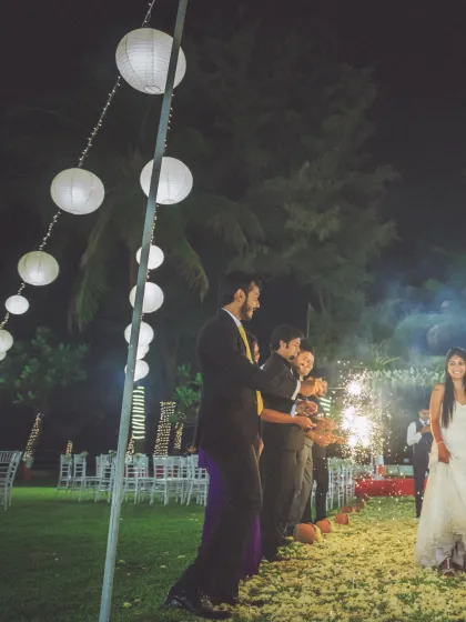 A wide shot of the bride's entrance at her outdoor evening reception. The guests with sparklers and the beautifully lit venue create a truly enchanting scene.