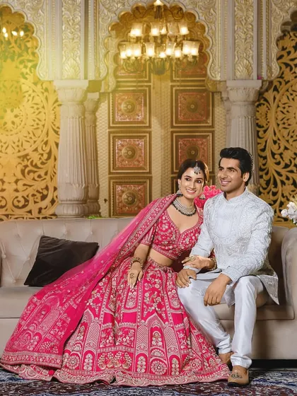 This is a perfect example of coordinated styling for a modern reception or engagement. The bride's vibrant pink lehenga is intricately detailed, and the groom's elegant white sherwani provides a beautiful contrast, creating a look that is both regal and contemporary.
