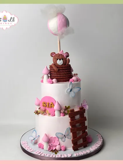 A fairytale cake for Sia's birthday, featuring a teddy bear in a hot air balloon, delicate butterflies, and a whimsical ladder.