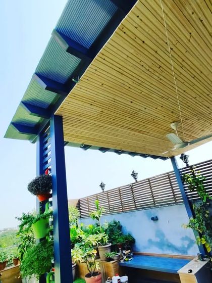 A beautiful pergola with a pine wood-clad ceiling and a duco-finished blue metal frame, creating a striking color combination.
