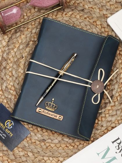 A blue leather thread-bound diary and pen set with a crown charm.