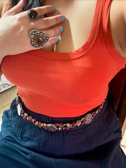 A close-up showing the details of the orange tank top and the beaded belt. The different colored rings add another layer of interest.