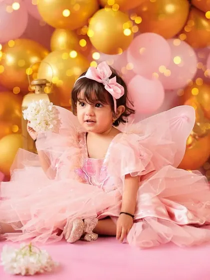 A little fairy princess in a magical setting. Dressed in a pink tulle dress with wings, she is surrounded by a wall of pink and gold balloons for her second birthday portrait.