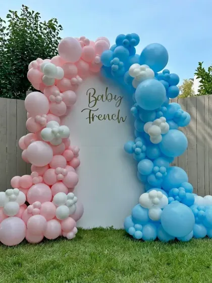 A simple and modern gender reveal backdrop for an outdoor party. The clean white panel is framed by asymmetrical balloon clouds in pink and blue, perfect for a garden or backyard celebration.