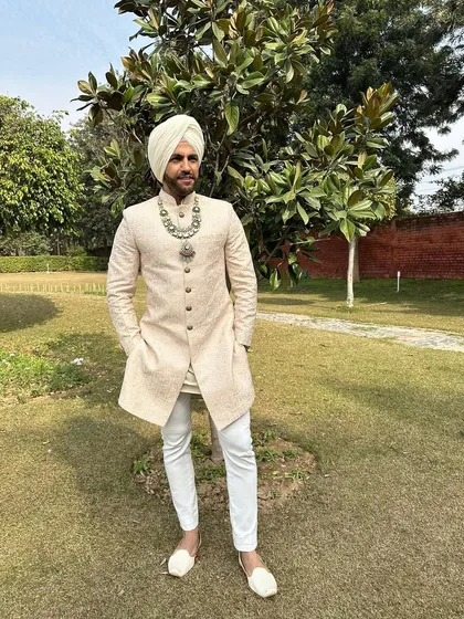A side profile of the Sikh groom ensemble, offering a better view of the sherwani's texture and the elegant drape of the turban.