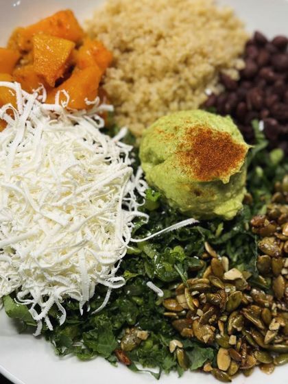 A vibrant and nutritious Buddha bowl with quinoa, roasted butternut squash, black beans, kale, shredded cheese, and guacamole.