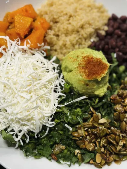 A vibrant and nutritious Buddha bowl with quinoa, roasted butternut squash, black beans, kale, shredded cheese, and guacamole.