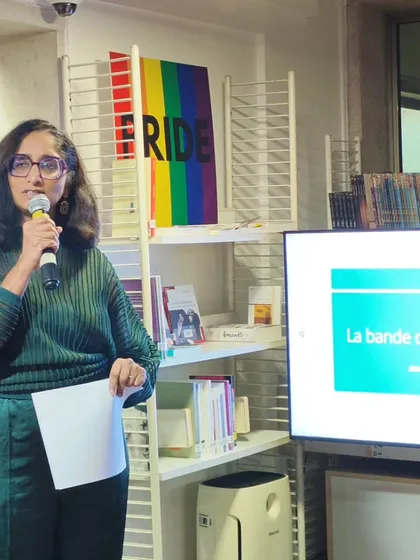 A member of our team introduces the speakers at the Quebec comics event, standing next to our library's PRIDE display. This shows how our values are integrated into all our activities.
