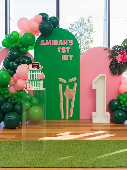 A closer view of the cricket-themed first birthday, highlighting the custom cake on a clear pedestal and the large light-up number '1'.