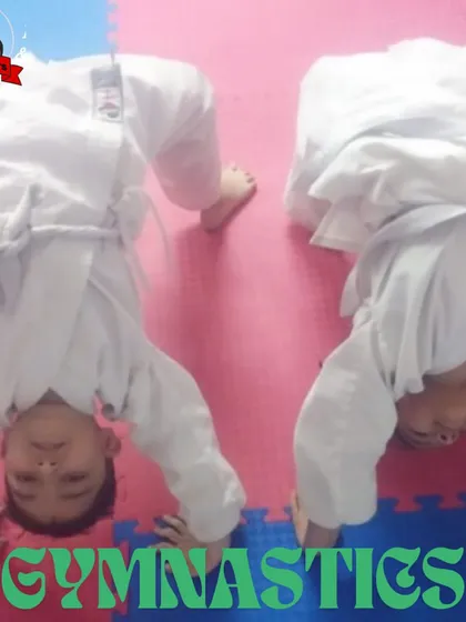 Two young students in their martial arts uniforms practice the initial phase of a headstand. This foundational acrobatic skill is key for developing spatial awareness and upper body strength.
