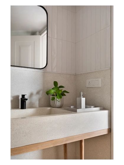 A close-up of a cast in-situ white terrazzo sink resting on a simple rubberwood base. The contrast between the smooth, speckled terrazzo and the vertical lines of the subway tiles behind it creates a subtle textural dialogue.
