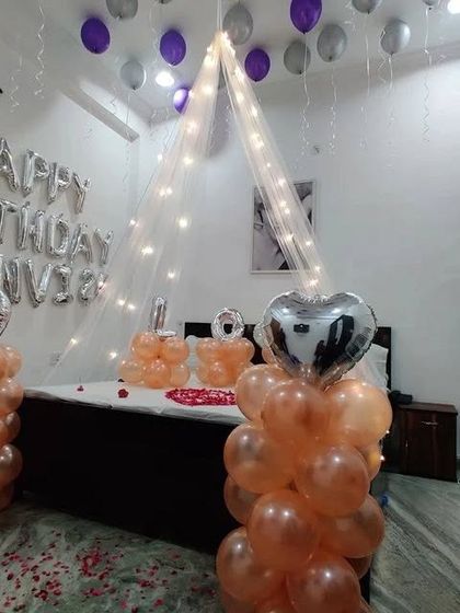 A wider view of the romantic room setup, showing balloon pillars and scattered petals on the floor.