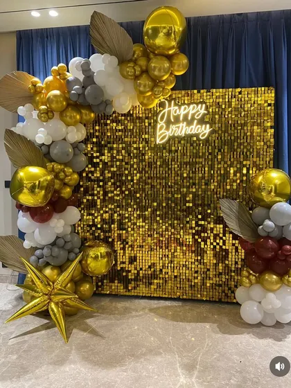 This glamorous birthday decoration features a brilliant gold sequin shimmer wall as the centerpiece. It is framed by an organic balloon garland with gold, grey, white, and maroon chrome balloons, creating a luxurious and festive look.