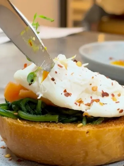 The perfect egg-cutting moment. A close-up of a knife slicing into a poached egg on our Smoked Salmon Benedict, revealing a runny yolk.