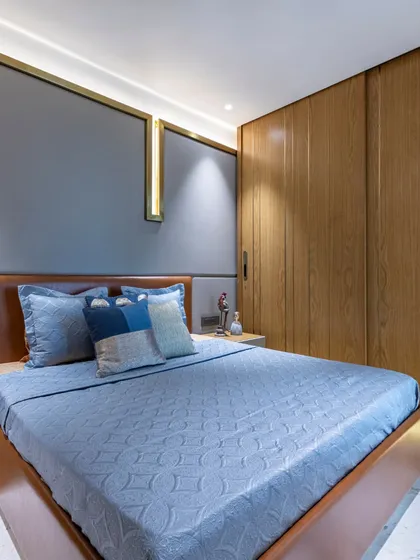 A full view of the bedroom in the Filigree House, showing the balance between the warm wood wardrobe, the cool grey wall panels, and the inviting bed. The space is a testament to modern, comfortable design.