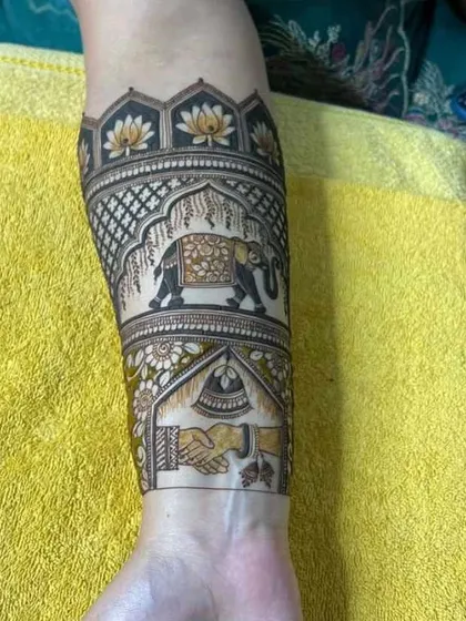 A close-up of a unique bridal arm design. It features a majestic elephant under a decorated arch and a depiction of the couple's hands joining, symbolizing their union.