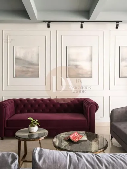 A living room from one of our featured projects, with a bold burgundy Chesterfield sofa set against a wall with classic molding. The mix of grey and burgundy upholstery creates a sophisticated and layered look.