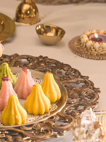 The vibrant colours of my assorted modaks on an ornate brass tray, set against a backdrop of festive decor.