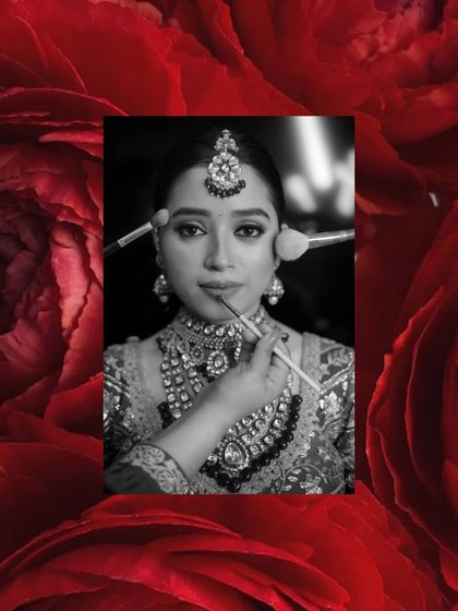 A black and white shot of a bride getting her makeup done, framed by a dramatic red floral border.